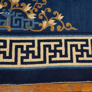 Low-pile navy blue rug with tan vines and a thick beige geometric key border resting on hardwood flooring.