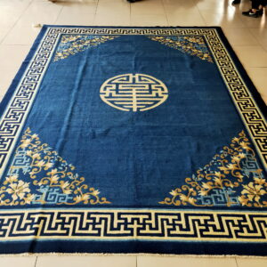 Deep blue rug with cream key border, gold floral corners, and a central circular motif on tile floor.