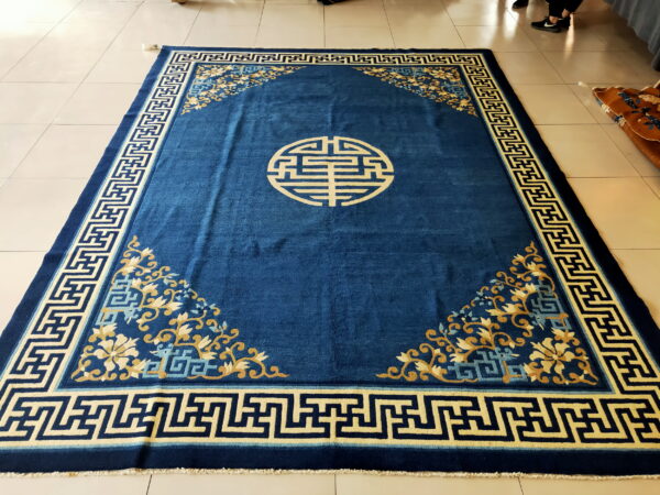 Deep blue rug with cream key border, gold floral corners, and a central circular motif on tile floor.