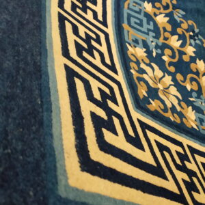 Close-up of a deep blue rug corner showing cream, gold, and light blue floral and geometric fretwork patterns.