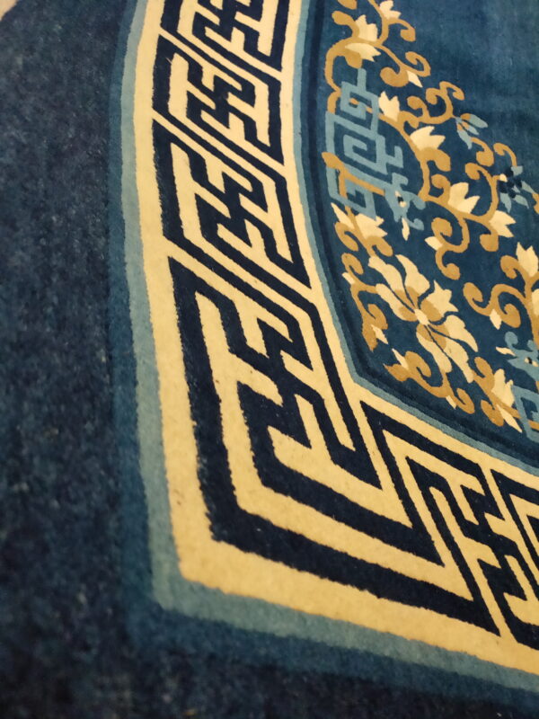 Close-up of a deep blue rug corner showing cream, gold, and light blue floral and geometric fretwork patterns.