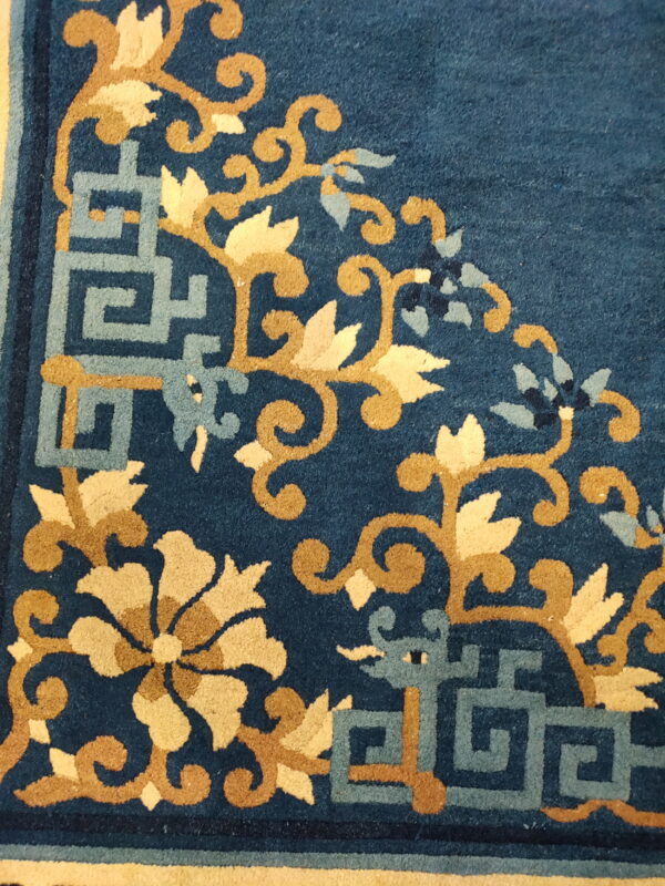 Deep blue rug texture with intricate tan floral scroll and light blue geometric corner designs.