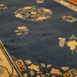 Deep blue rug featuring tan and light blue floral patterns and geometric motifs on a wood floor.