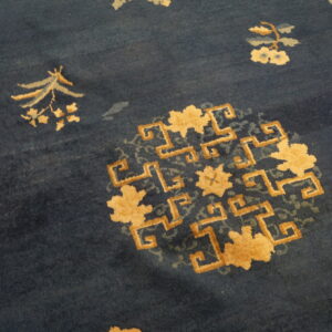 Low-pile navy rug with tan and pale blue floral sprays and a central geometric medallion design.