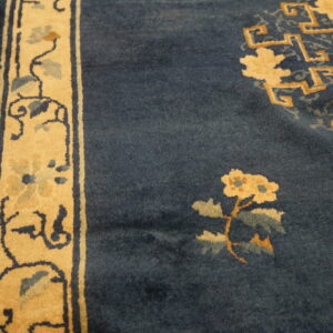 Dark blue rug with gold floral and geometric patterns, showing a tan border on hardwood flooring.