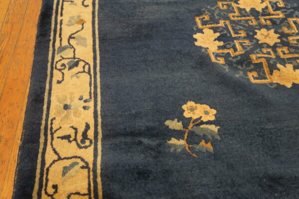 Dark blue rug with gold floral and geometric patterns, showing a tan border on hardwood flooring.