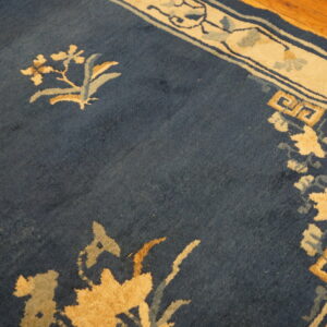 Navy blue rug field with gold and light blue floral motifs and a wide cream border on wood planks.