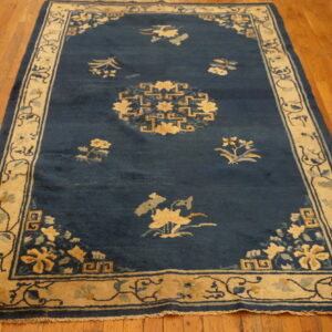 Dark blue rug with tan floral motifs and geometric borders rests on polished wood plank flooring.