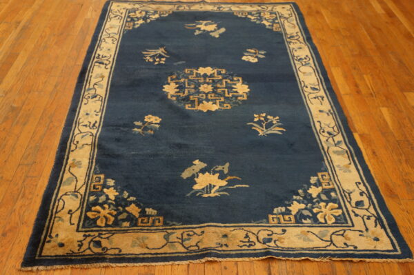 Dark blue rug with tan floral motifs and geometric borders rests on polished wood plank flooring.