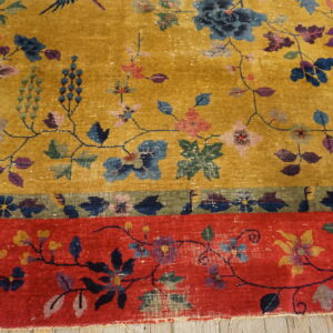 Mustard yellow rug featuring intricate blue and purple florals and a prominent red and green border on wood.