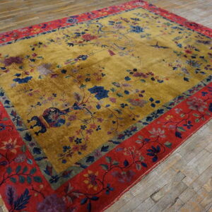 Golden yellow rug with scattered floral motifs and wide red borders rests on distressed wood planks.