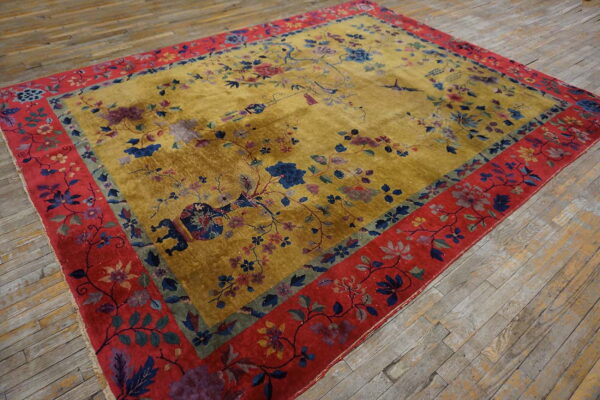 Golden yellow rug with scattered floral motifs and wide red borders rests on distressed wood planks.