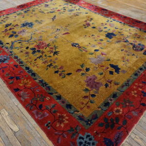 Plush yellow rug featuring blue and pink floral patterns bordered by wide red banding on wood floors.