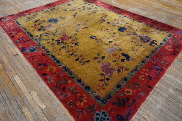 Plush yellow rug featuring blue and pink floral patterns bordered by wide red banding on wood floors.