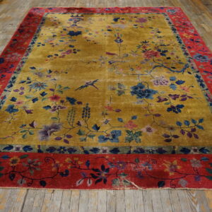 Gold floral rug with blue accents and a wide red border lying on distressed wood floorboards.