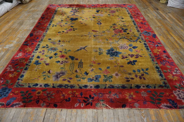 Gold floral rug with blue accents and a wide red border lying on distressed wood floorboards.
