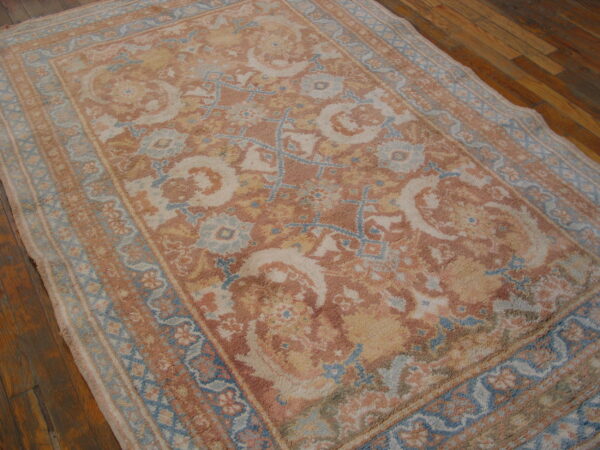 Textured rug featuring ornate patterns in muted terracotta, pale blue, and cream on a plank wood floor.