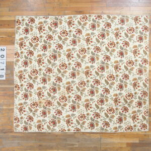 Cream rug with a repeating pattern of rust, gold, and green floral motifs laid on wide wooden floor planks.