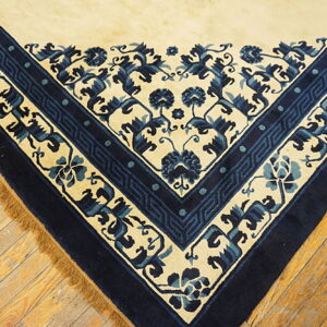 Cream and navy blue patterned rug corner on aged wood flooring with visible fringes.