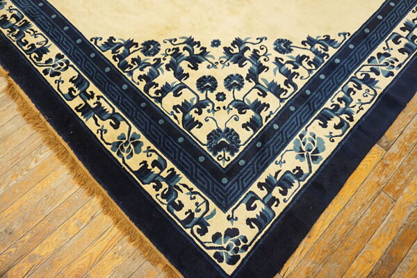 Cream and navy blue patterned rug corner on aged wood flooring with visible fringes.
