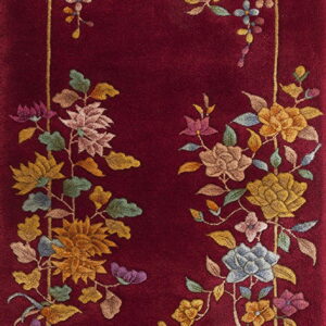 A deep red rug with a plush pile features a detailed, multi-colored floral vine border pattern.