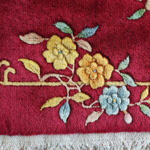 Raised floral design in yellow and blue against a deep red background with visible cream fringe.