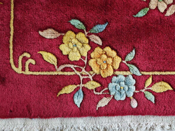 Raised floral design in yellow and blue against a deep red background with visible cream fringe.