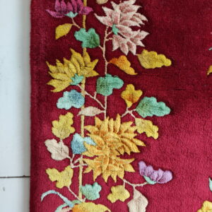 A plush, deep red rug features a raised, vibrant floral and vine design on white flooring.
