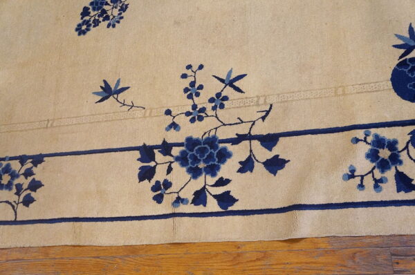 A beige rug with deep blue floral patterns and borders rests on rustic wooden plank floors.