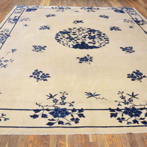 Cream rug featuring a large blue floral center and border, resting on wide wood plank flooring.