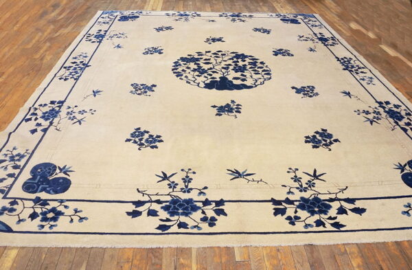 Cream rug featuring a large blue floral center and border, resting on wide wood plank flooring.