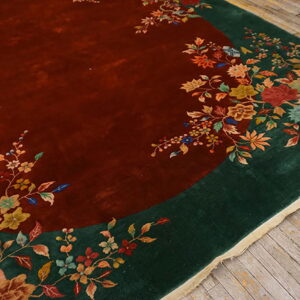 Rust field rug with a dark green border and colorful floral motifs laid on gray wooden planks.