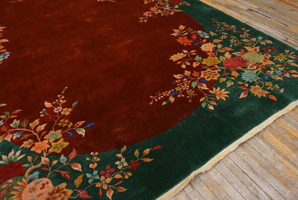 Rust field rug with a dark green border and colorful floral motifs laid on gray wooden planks.