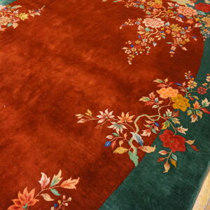 Rust red field rug with a dark green border and multicolor floral pattern on wood floor.