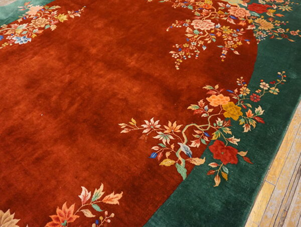 Rust red field rug with a dark green border and multicolor floral pattern on wood floor.