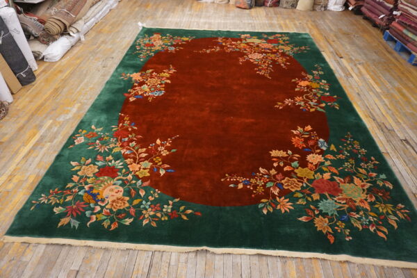 Large high-pile rug with a rust red center and dense multicolored floral patterns on a dark green border.