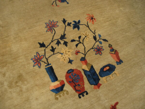 Medium pile tan rug detail showing blue and red stylized flowers and vessels on winding stems.