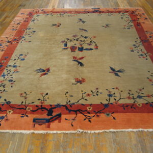 Beige and coral rug featuring branches, flowers, and flying birds, displayed on hardwood flooring.