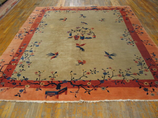 Beige and coral rug featuring branches, flowers, and flying birds, displayed on hardwood flooring.