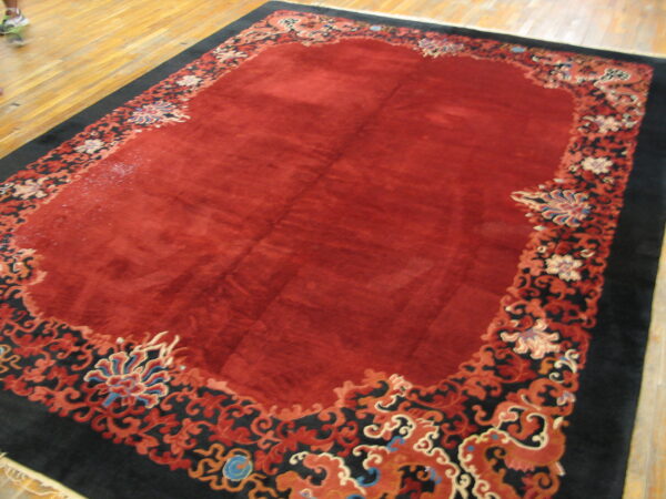 Deep red rug with an ornate black, orange, and blue floral border rests on a light wood floor.
