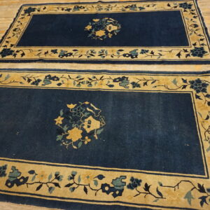 Matching dark blue rugs with gold floral borders lie side-by-side on light wooden planks.