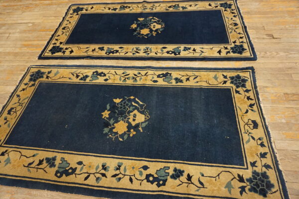 Matching dark blue rugs with gold floral borders lie side-by-side on light wooden planks.