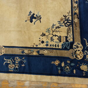 A beige rug with dense navy and taupe decorative borders featuring intricate floral patterns rests on wood floors.