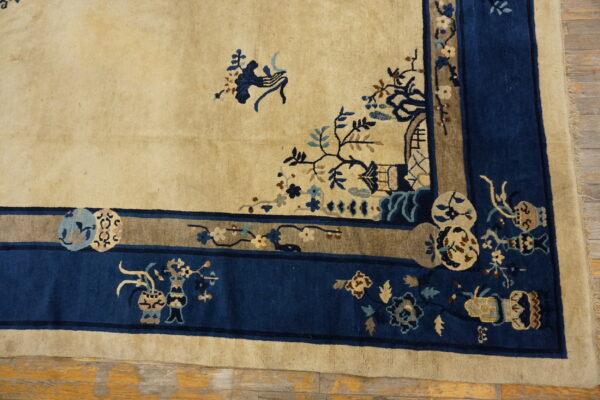 A beige rug with dense navy and taupe decorative borders featuring intricate floral patterns rests on wood floors.