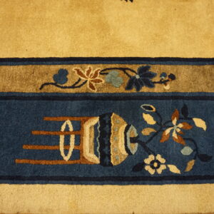 A close-up shows a gold rug field bordering deep blue bands with stylized floral and vase motifs.