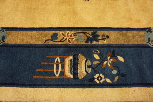 A close-up shows a gold rug field bordering deep blue bands with stylized floral and vase motifs.