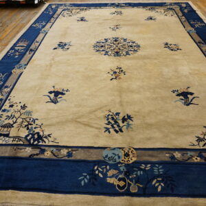 A large cream rug featuring blue traditional floral and scenic motifs rests on light brown wood flooring.