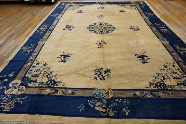 A large cream rug featuring blue traditional floral and scenic motifs rests on light brown wood flooring.