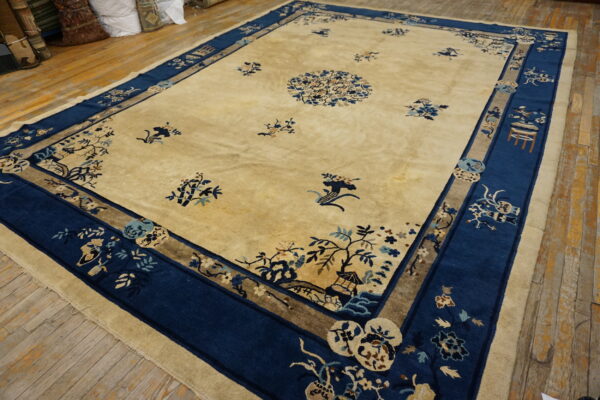 Large beige rug with deep blue borders and intricate botanical motifs lying on rough wooden planks.