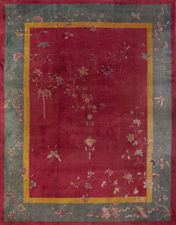 Red field rug with a sage border featuring sprawling multi-colored floral and butterfly designs.